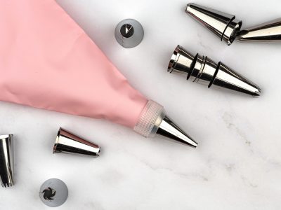 Pastry bag cream pink injector for cake dessert decoration Pastry bag cream pink injector for cake dessert decoration, supplies kit icing piping, stainless steel nozzle tips. DIY tools on white marble background. Cooking bakery concept with copy space